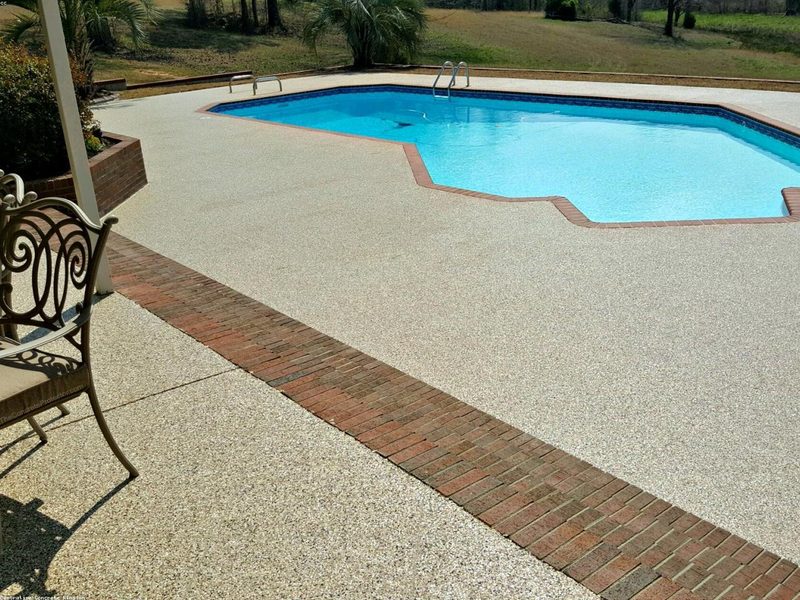 Exposed aggregate concrete pool deck with brick border around an in-ground pool